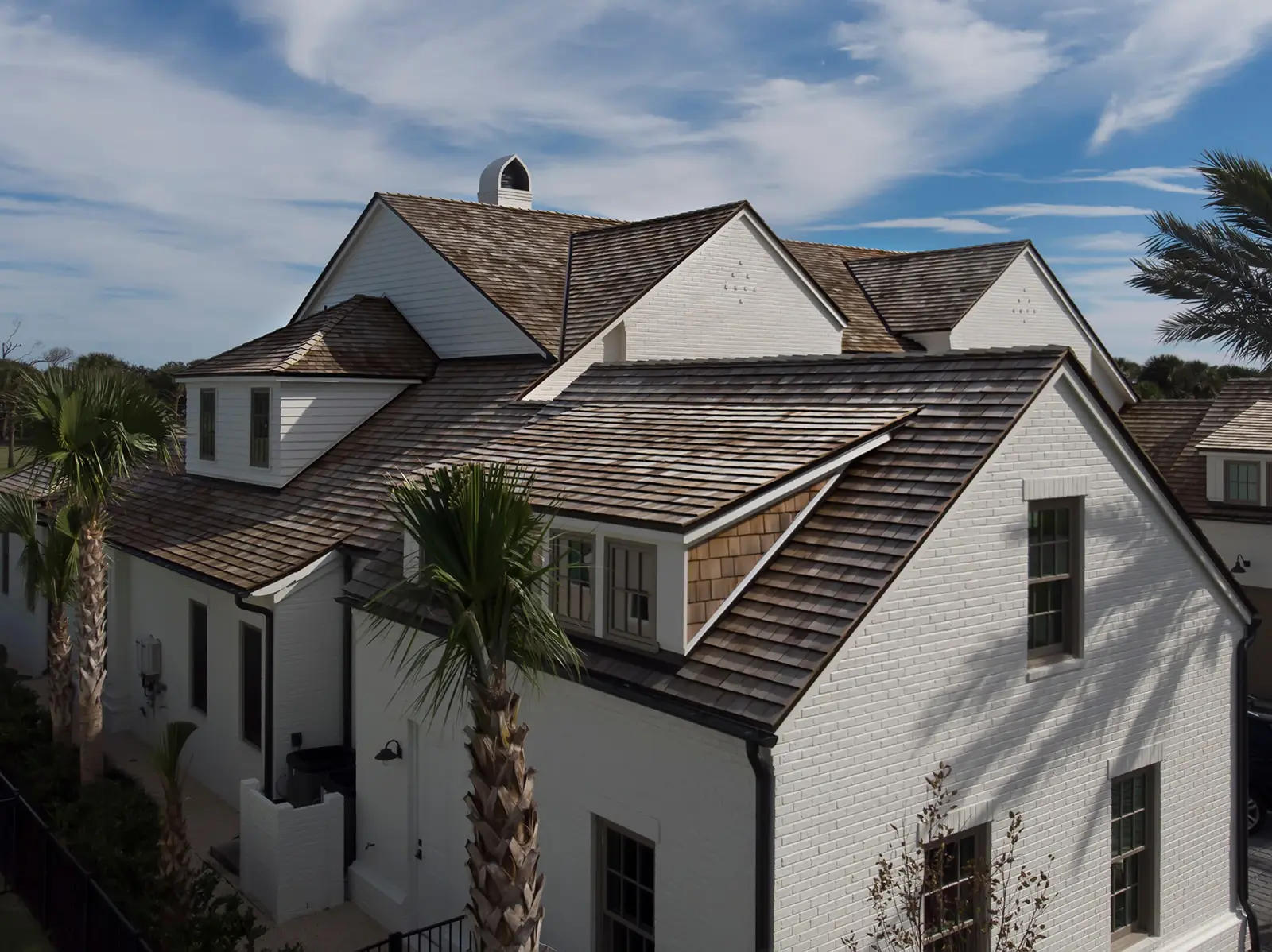 Aerial view of a shake-style roof with dormers and a chimney on a white brick home in the Jacksonville area, serviced by Cache Roofing