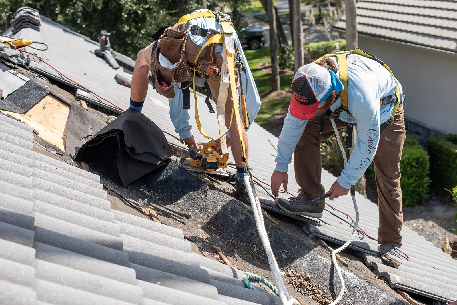 Two Cache Roofing crew members in safety harnesses replacing underlayment beneath concrete roof tiles on a Jacksonville home