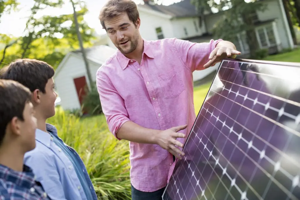 Two children and a young man looking at solar panels